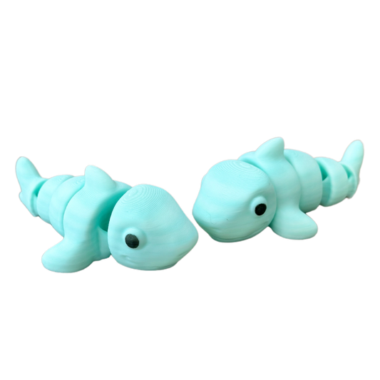 A small shark fidget toy with a blue-to-white gradient body, black eyes, and flexible articulation for sensory play