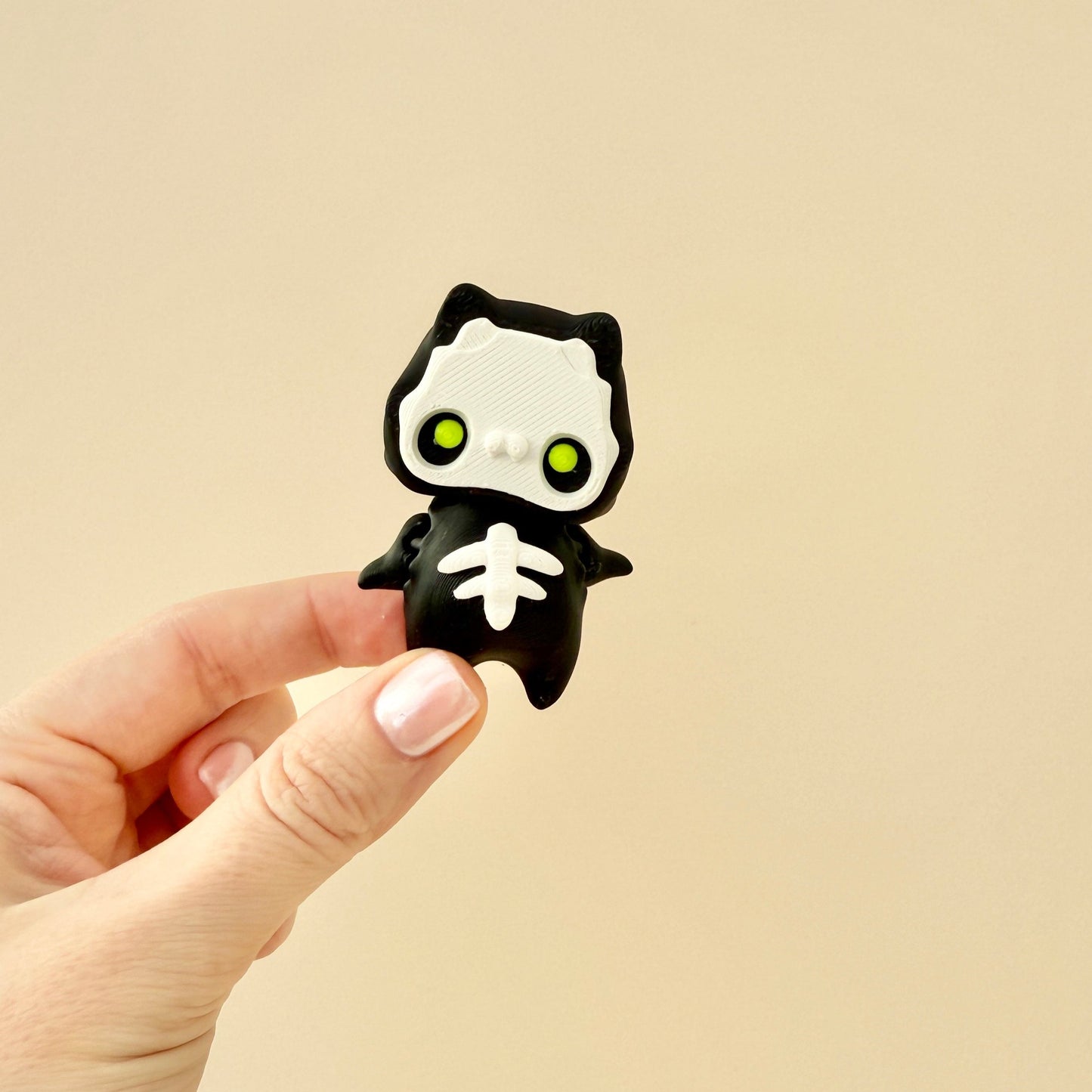 Compact Pixie-Skelly fidget toy featuring a black design with white details and bright lime green eyes.