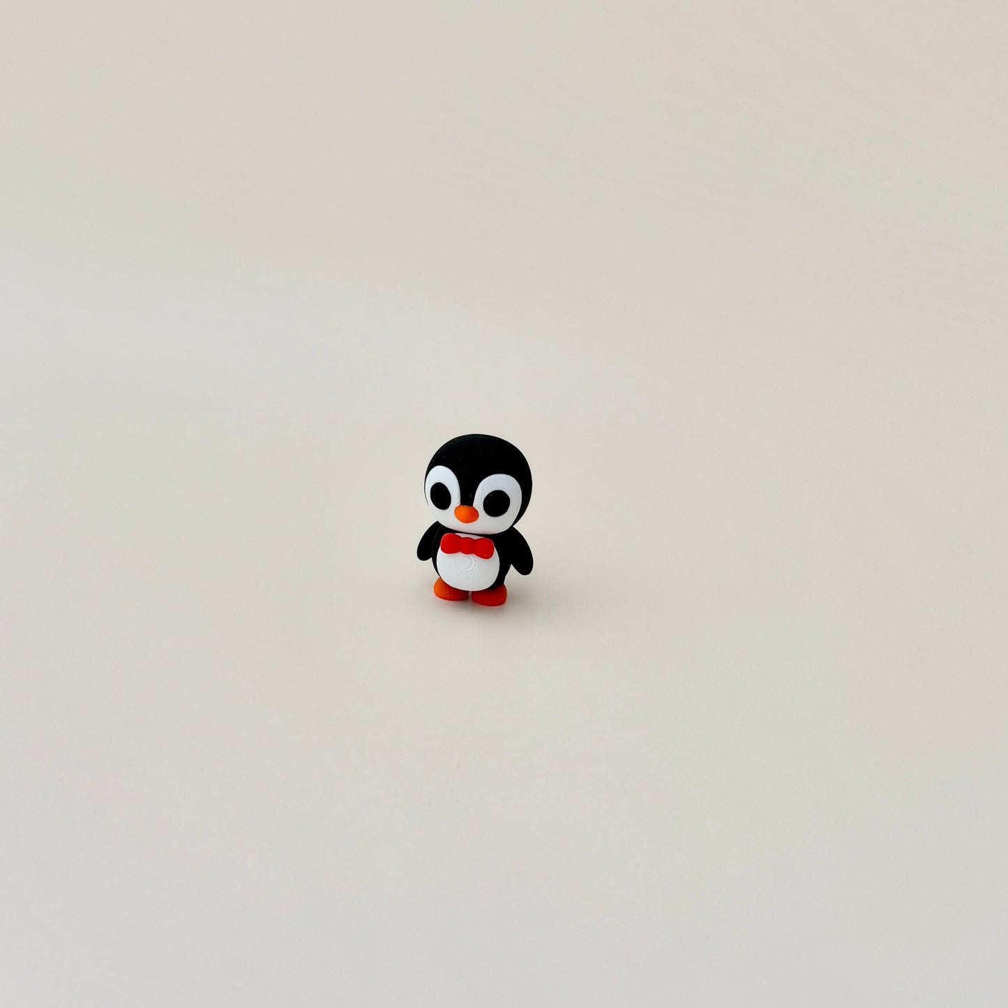 4cm penguin fidget with wobbly head, black and white body, orange details, and a red bow tie.