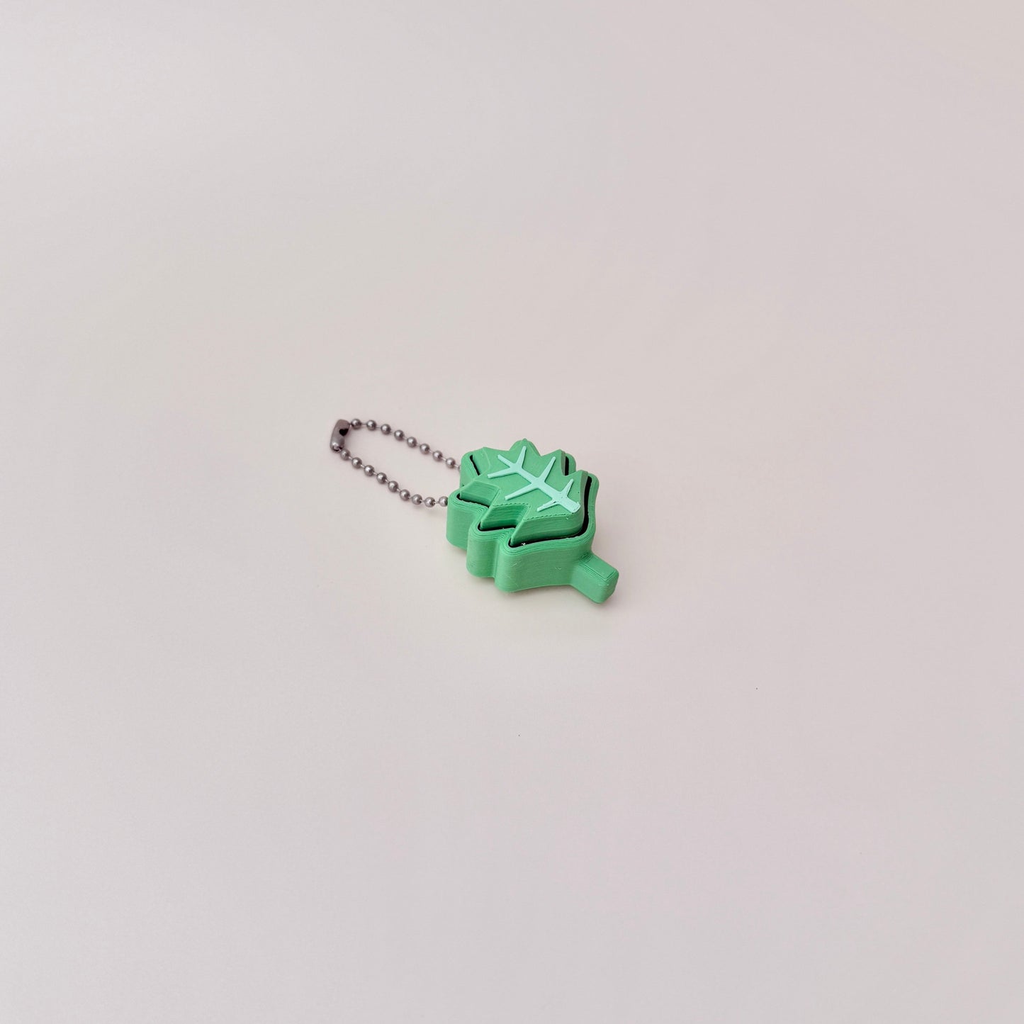 Green holly leaf fidget toy with clicking motion, attached to a keychain for easy carrying, 4cm in size.