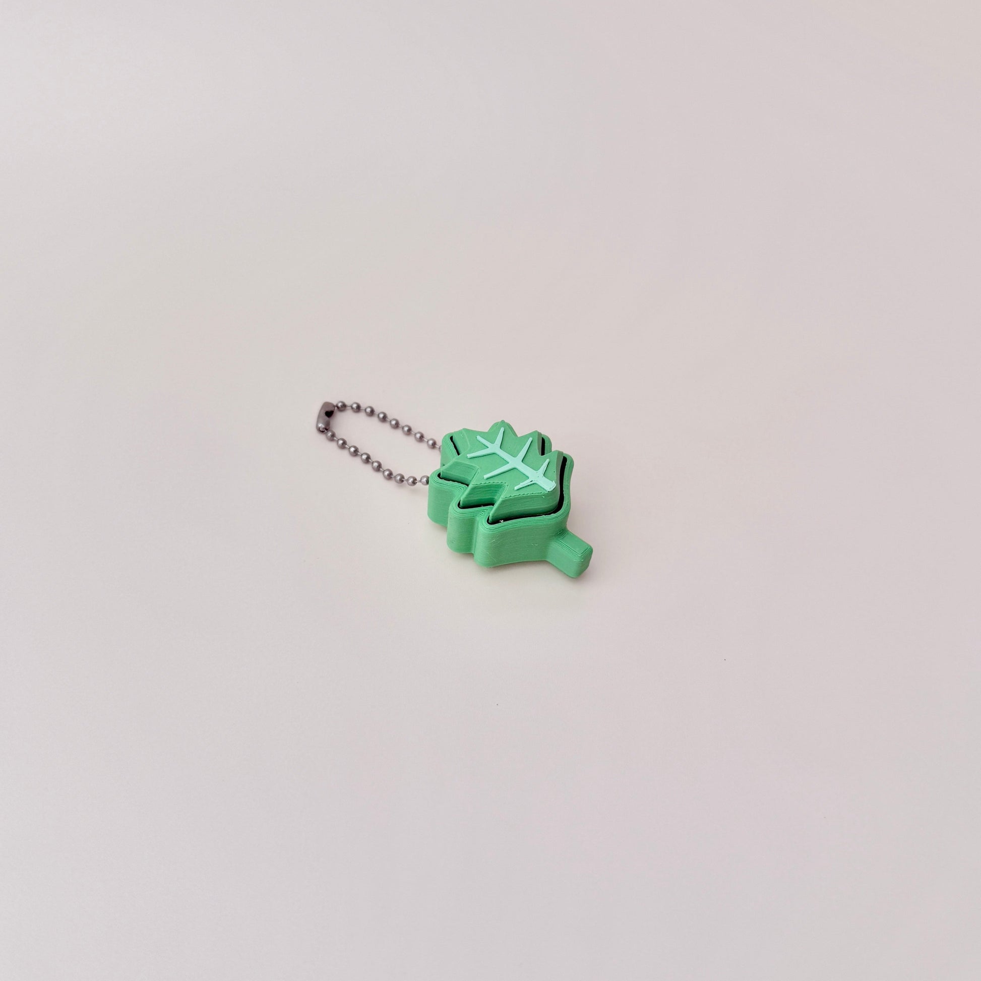 Green holly leaf fidget toy with clicking motion, attached to a keychain for easy carrying, 4cm in size.