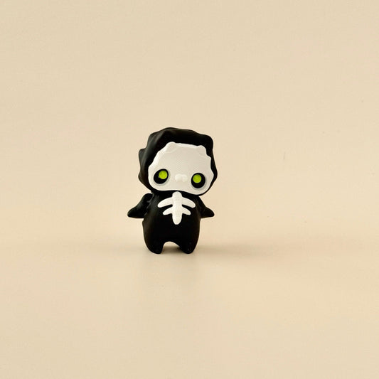 Pixie-Skelly fidget toy with black body, white face and ribs, and fluorescent lime green eyes.