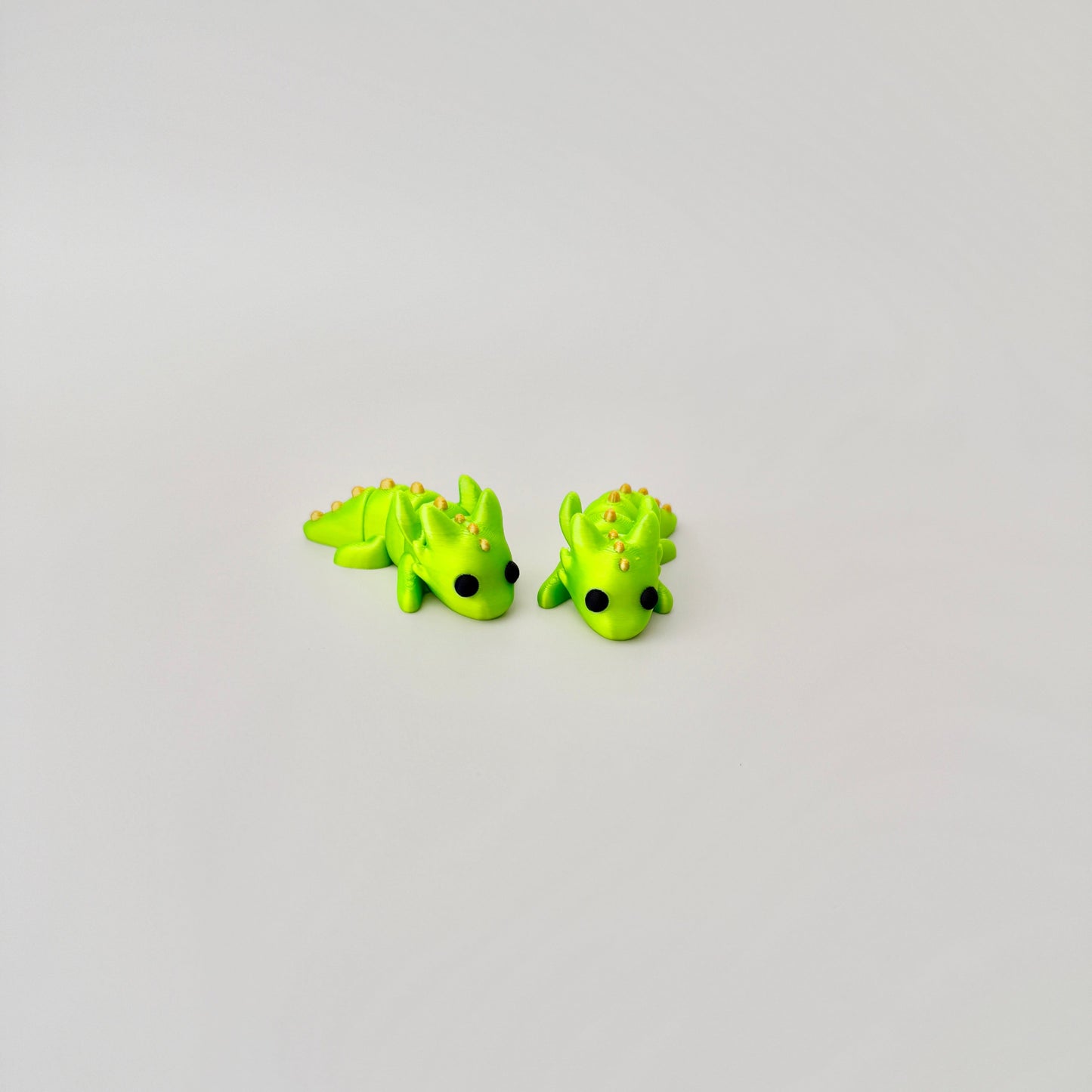 Luminous lime green baby dragon fidget toy, featuring black eyes and gold detailing, fully articulated.